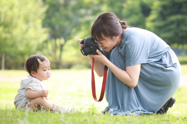 芝生の上に座っている赤ちゃんをママがカメラで撮影している